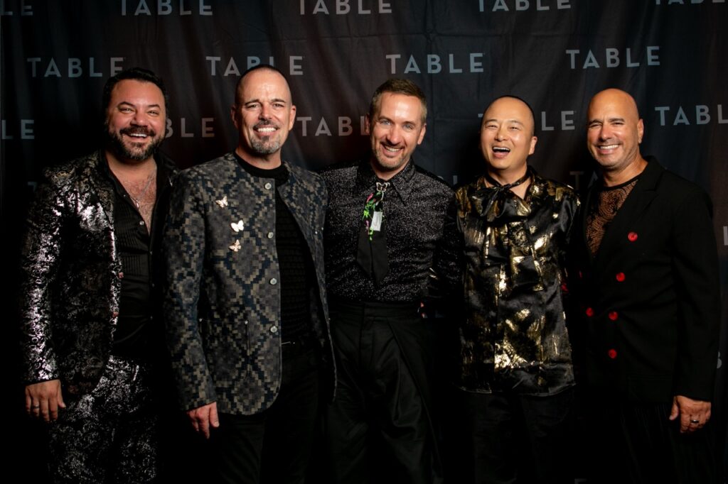 Five men in stylish, sparkly outfits pose for a photo.