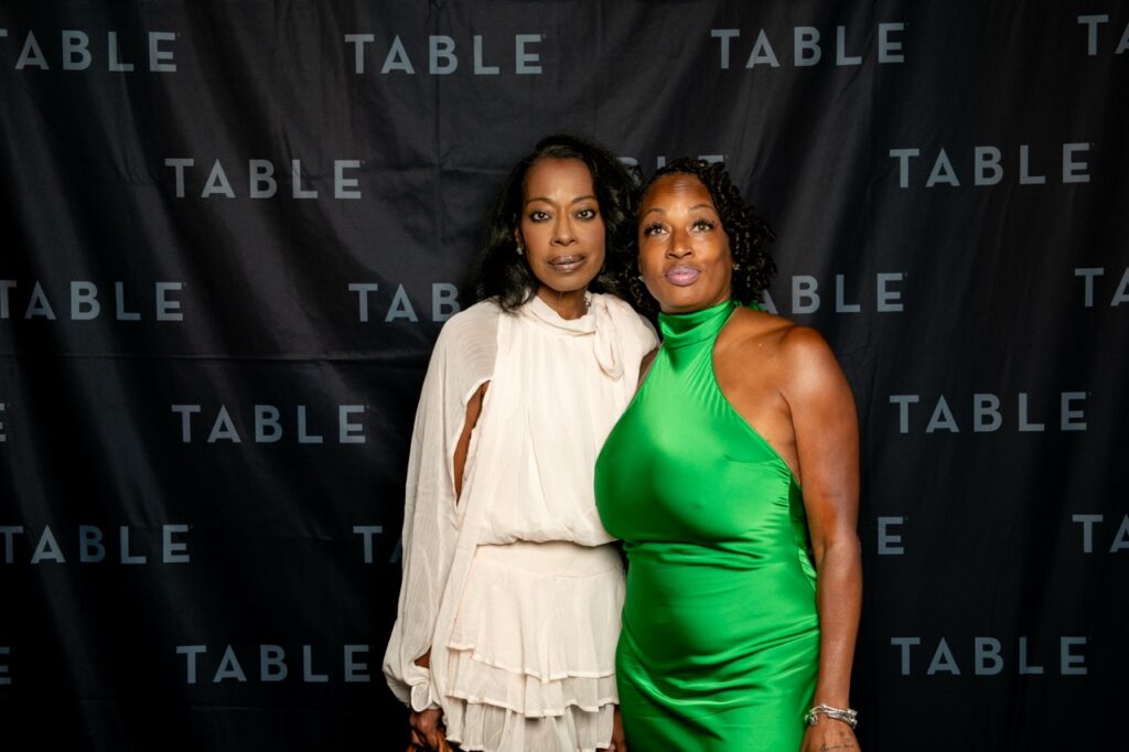 Two women posing for a photo at an event with a "TABLE" backdrop.