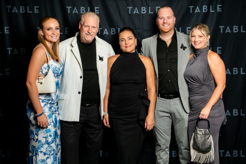 Five people pose for a photo at a TABLE event, dressed in formal attire.