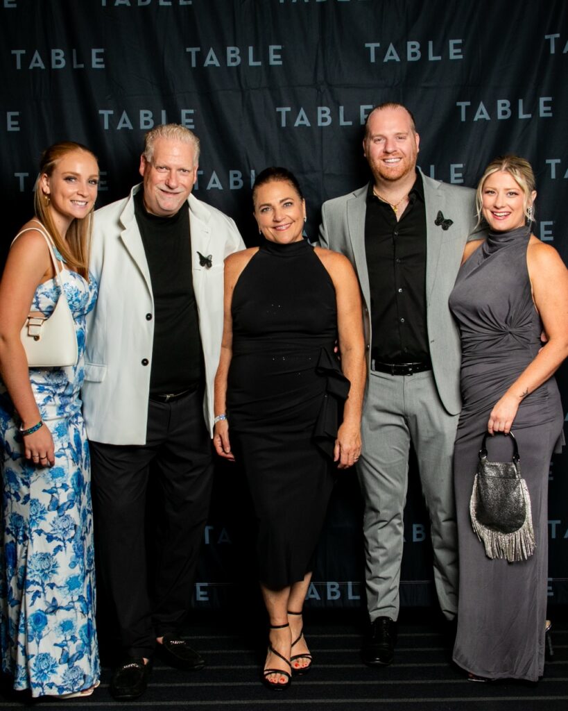 Five people posing for a photo in front of a backdrop with the word "TABLE" repeated.