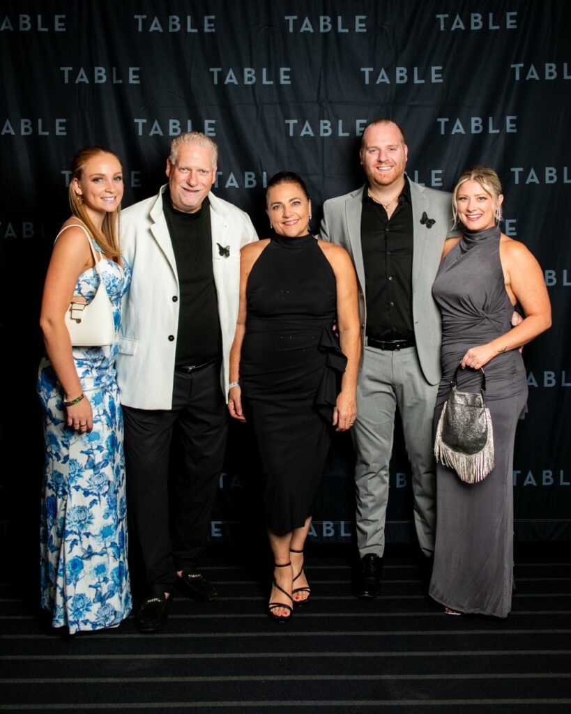 Five people posing for a photo at an event with a "TABLE" backdrop.