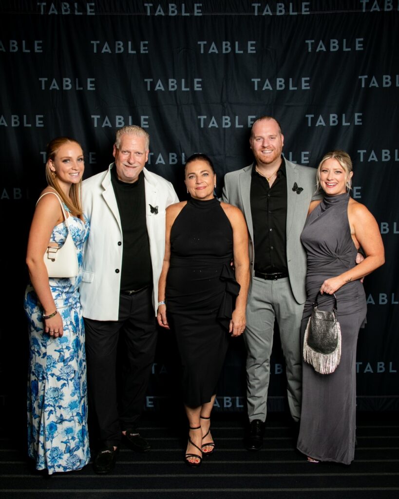 Five people pose for a photo in front of a black backdrop with "TABLE" logos.