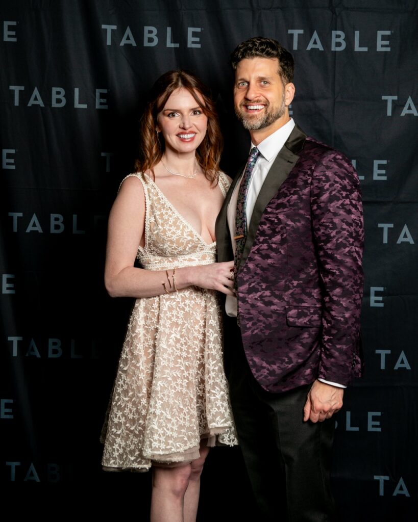 Couple posing in front of a "TABLE" backdrop at an event.