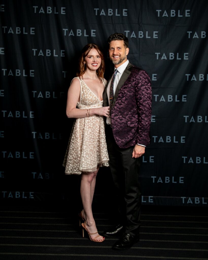Couple posing in front of a TABLE backdrop at an event