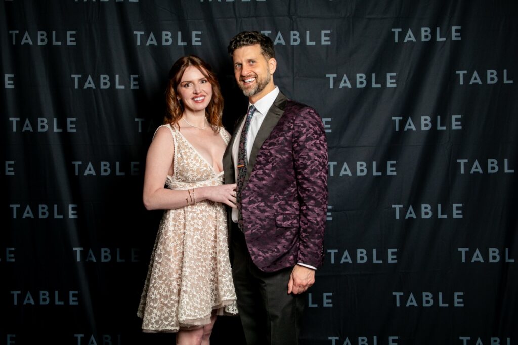 Couple posing in front of a "TABLE" backdrop at an event