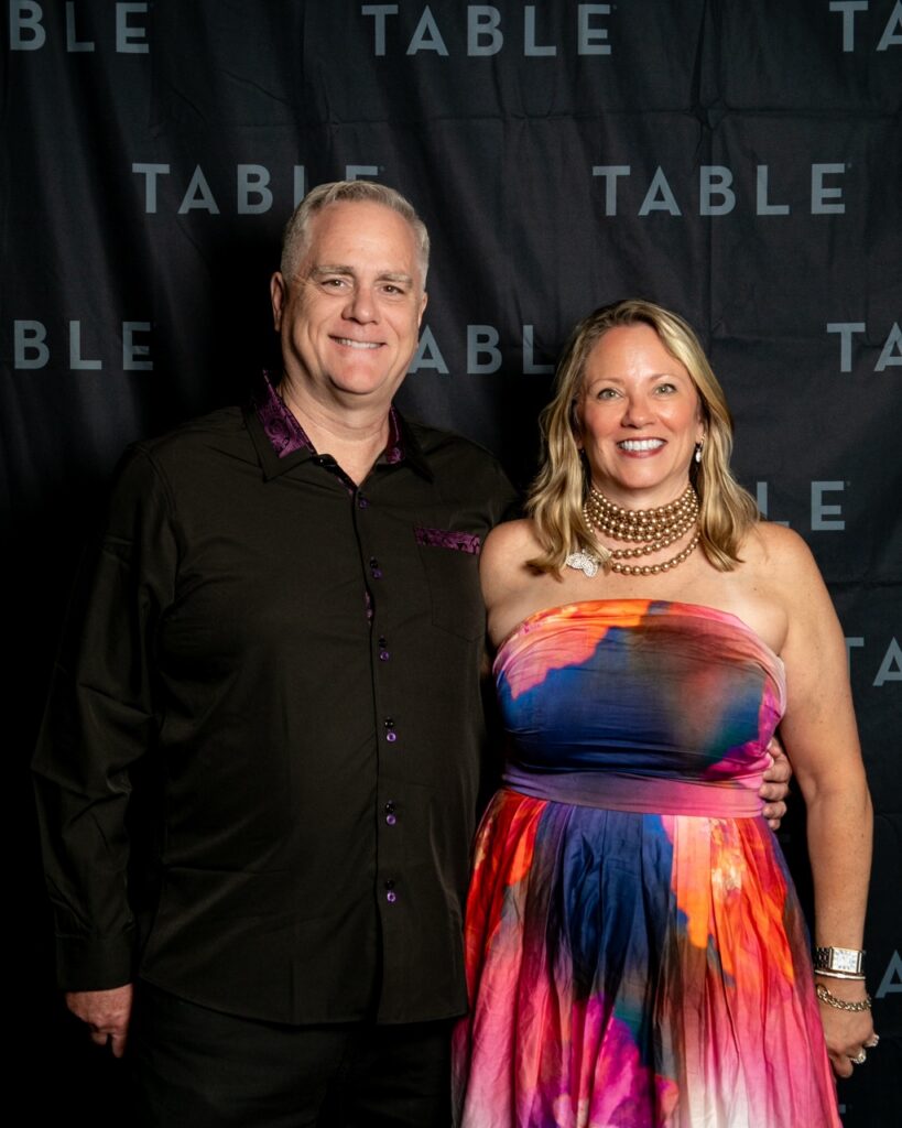 Couple posing in front of a black backdrop with "TABLE" logo