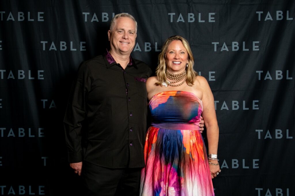 Couple posing for a photo in front of a black backdrop with "TABLE" logos.
