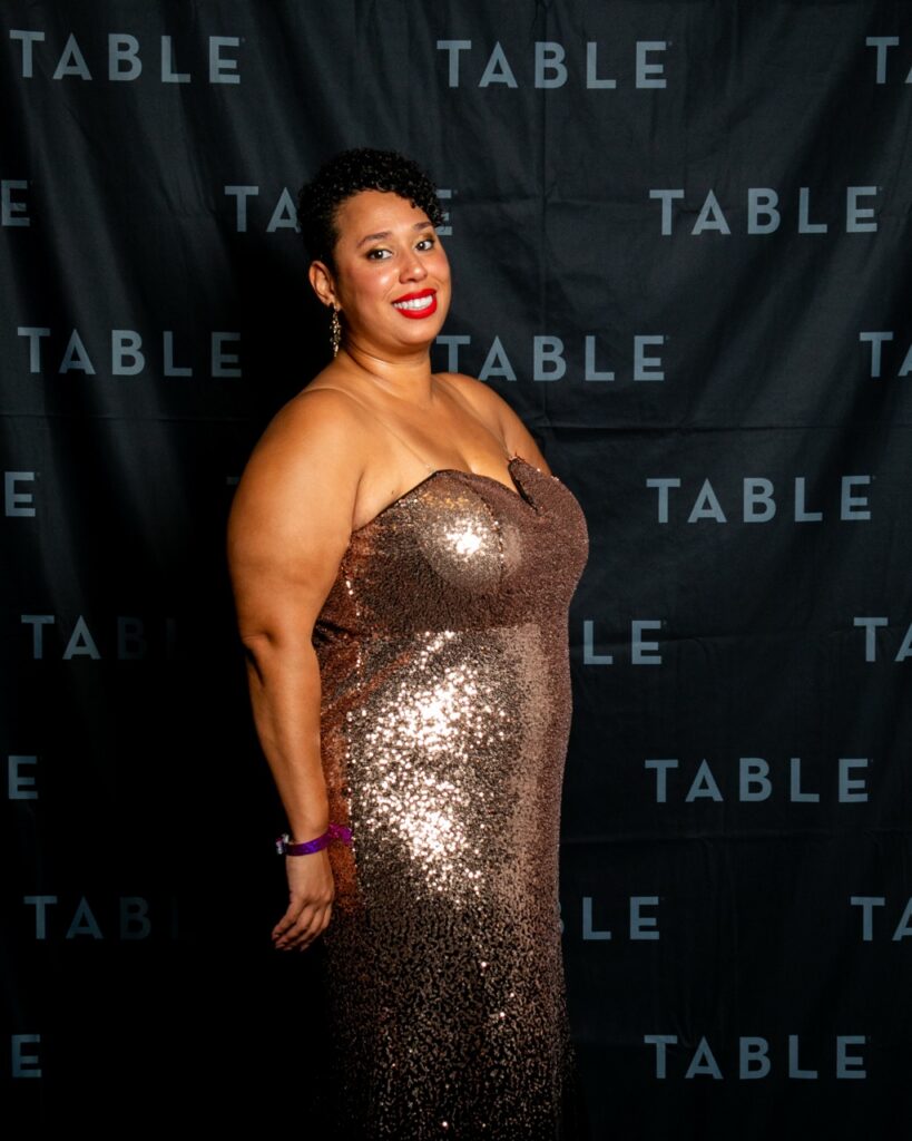 Woman in a gold sequin dress smiles at a TABLE event
