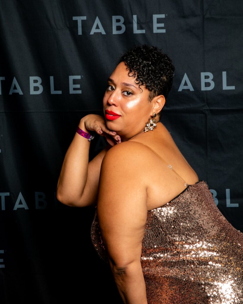 Woman in sequined dress posing against a black "TABLE" backdrop