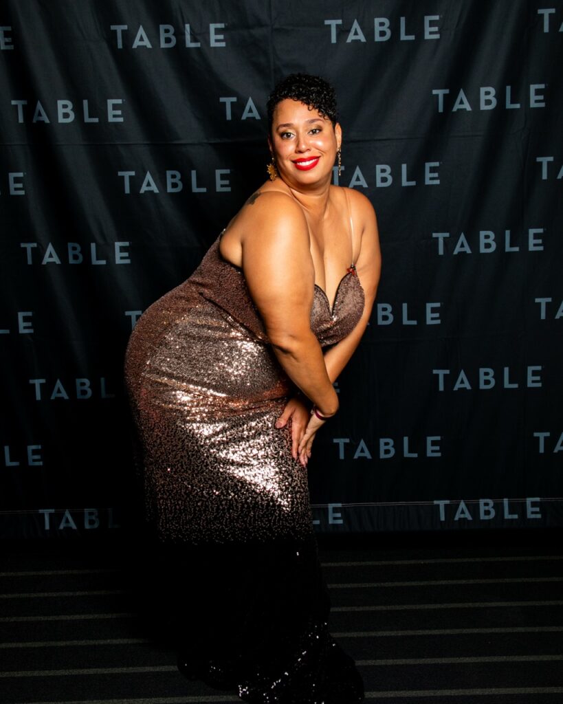 Woman in a sparkly rose gold and black dress poses at a TABLE event