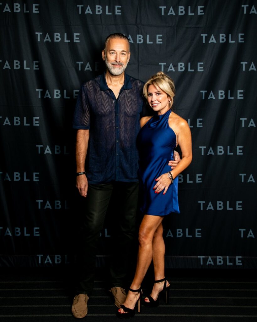 Couple posing in front of a TABLE backdrop at an event