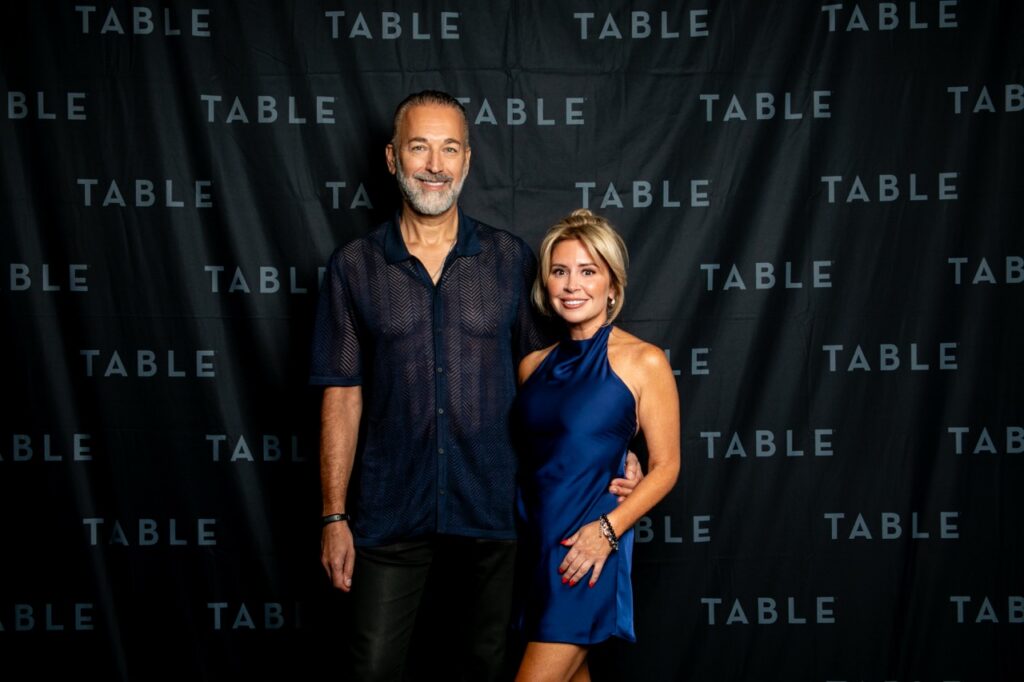 Couple posing in front of a black backdrop with "TABLE" repeated