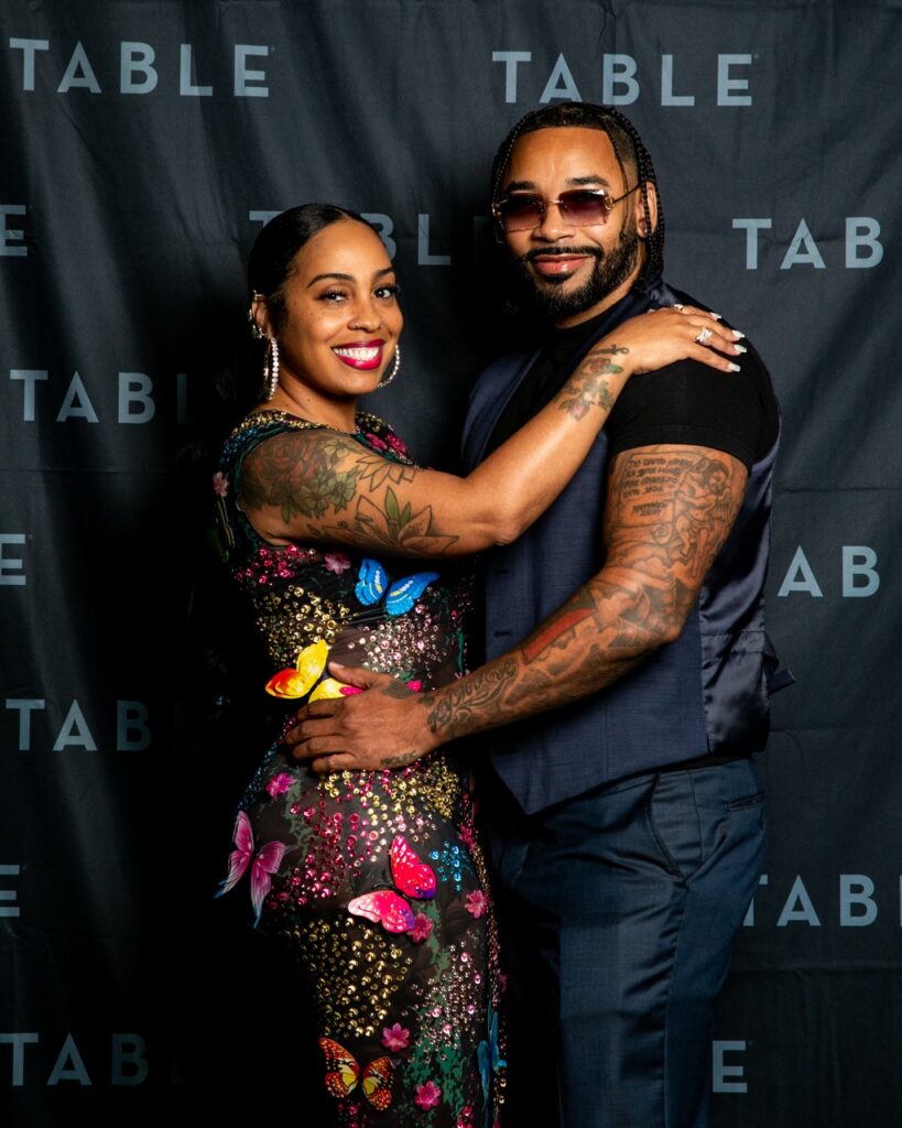 Couple posing in front of a black backdrop with "TABLE" logo