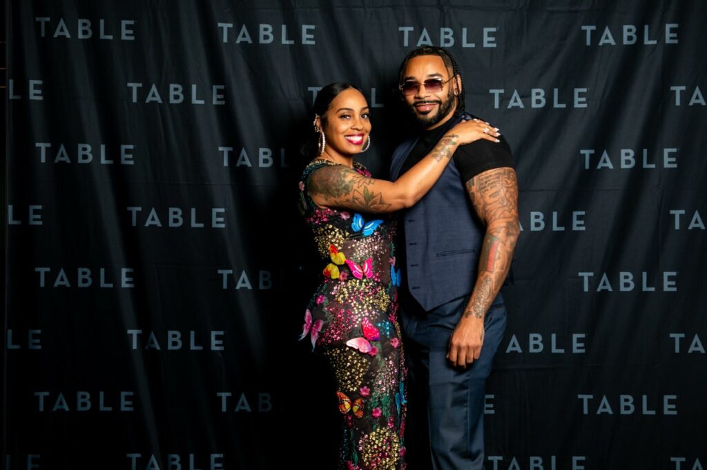 Couple posing for a photo at an event with a "TABLE" backdrop.