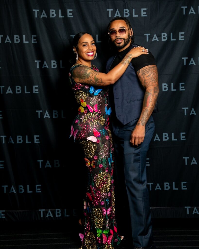 Couple poses in front of a black backdrop with "TABLE" logo.