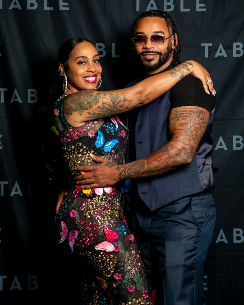 Couple posing for a photo at an event, woman in butterfly dress, man in vest.