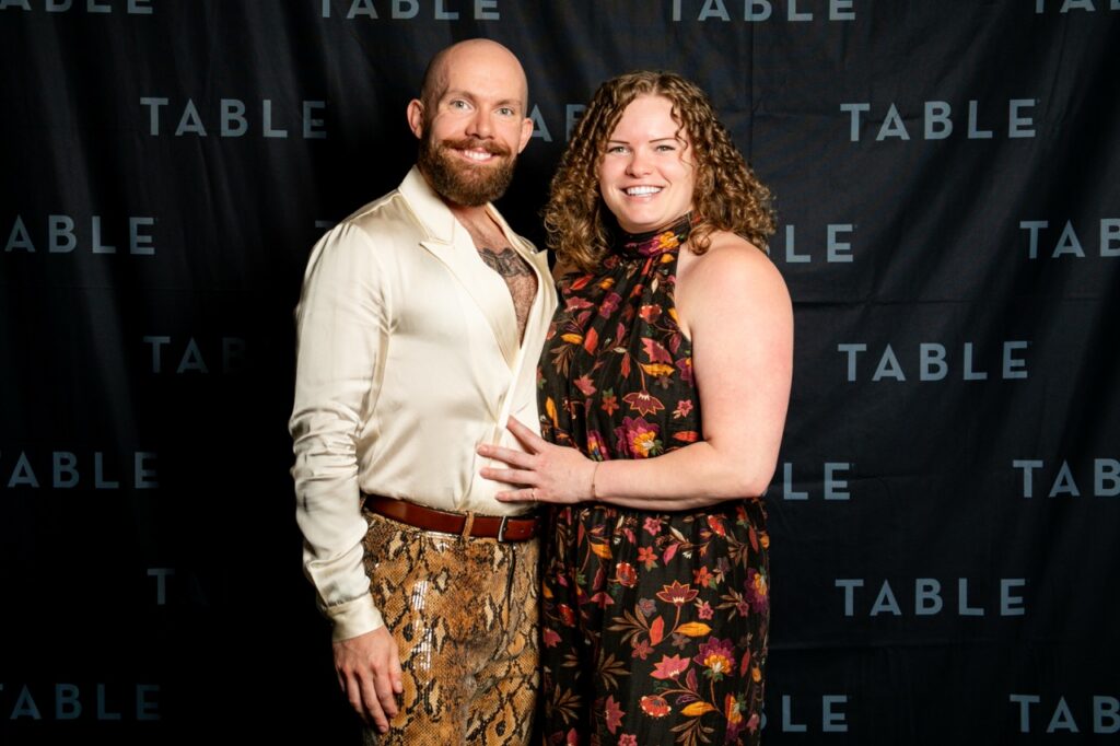Couple posing in front of a black backdrop with "TABLE" logo