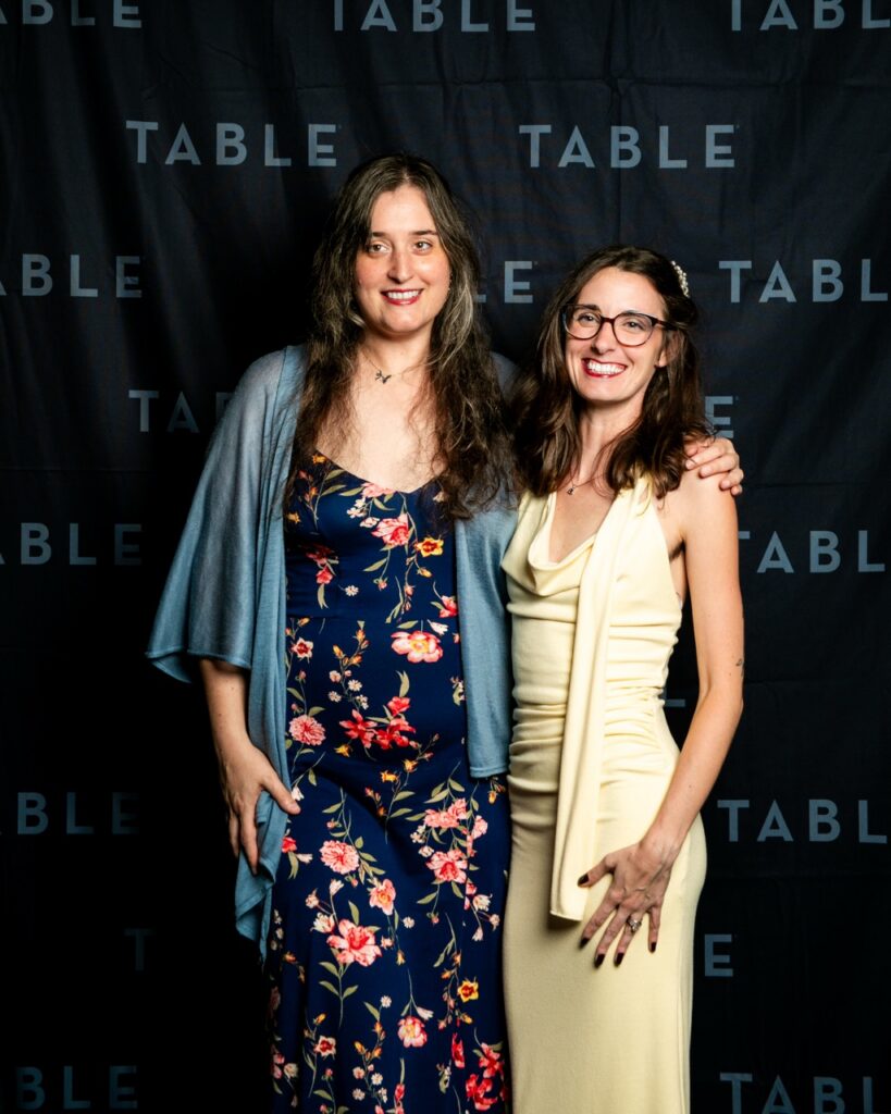 Two women in formal dresses pose for a photo at a TABLE event.
