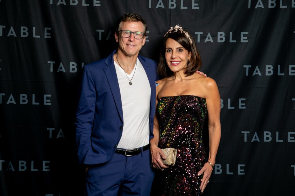 Couple in formal wear posing in front of a backdrop with "TABLE" repeated