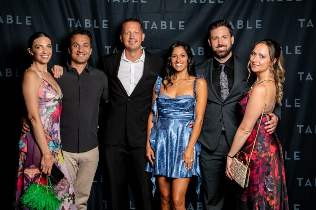 Six stylish adults pose for a photo at a TABLE event, with the TABLE logo visible.