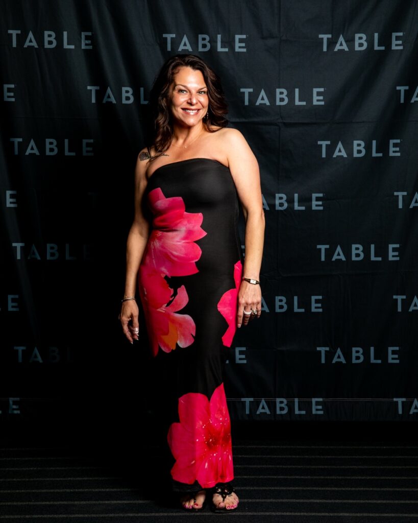 Woman in strapless floral dress poses in front of a "TABLE" backdrop