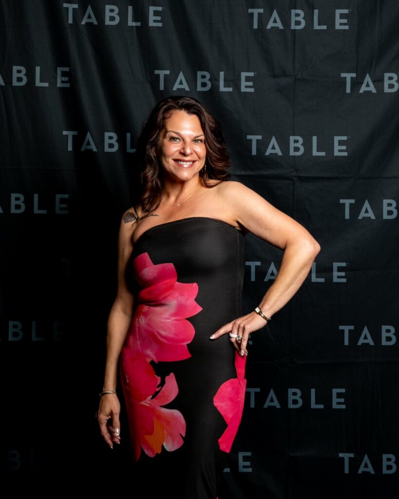 Woman in a strapless floral dress poses in front of a black backdrop with "TABLE" logo.