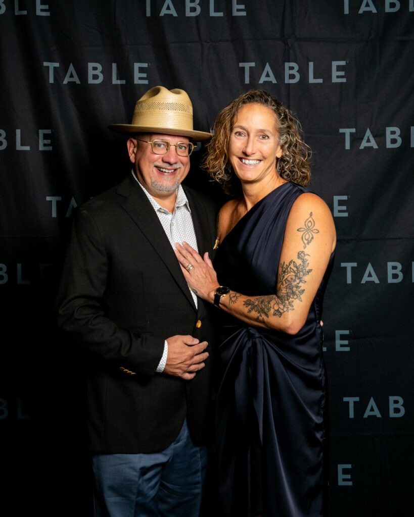 Couple smiling at the camera in front of a TABLE backdrop