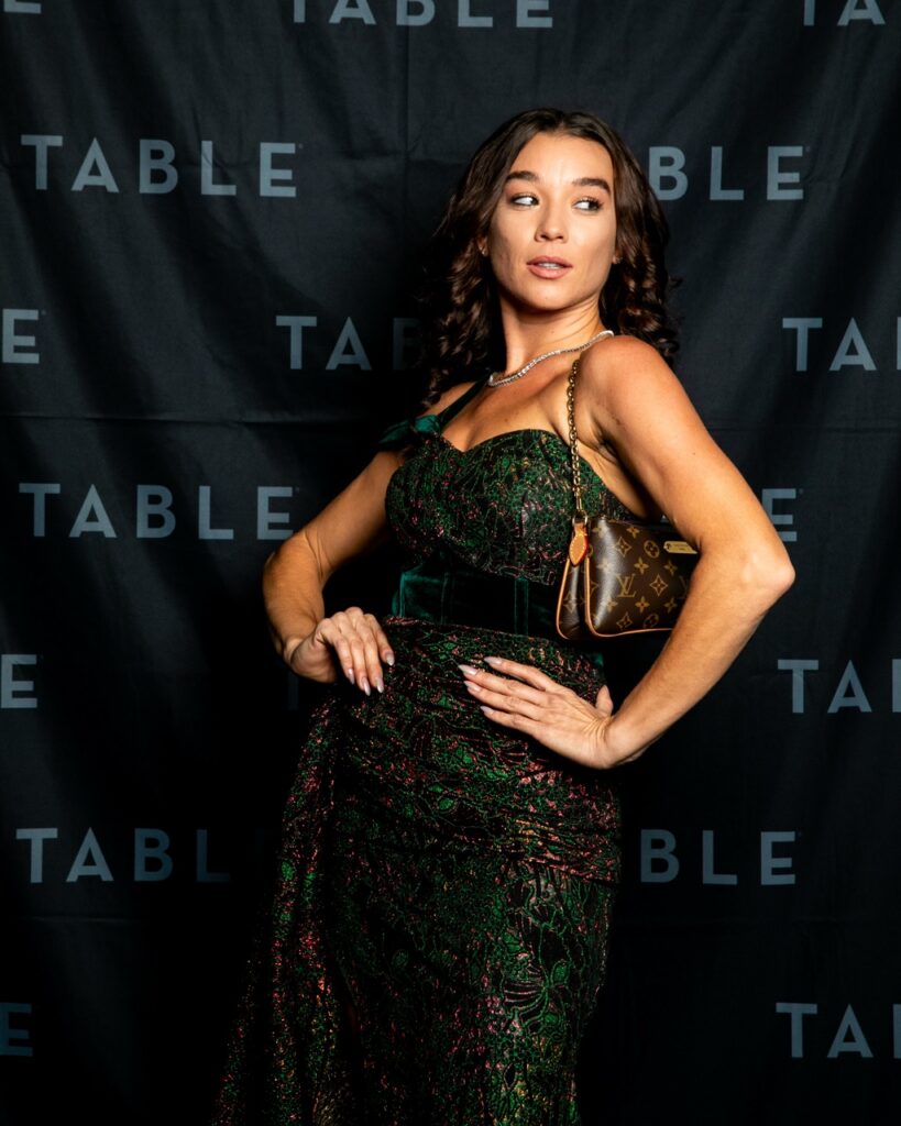 Woman in a sparkly green dress poses with a designer handbag.