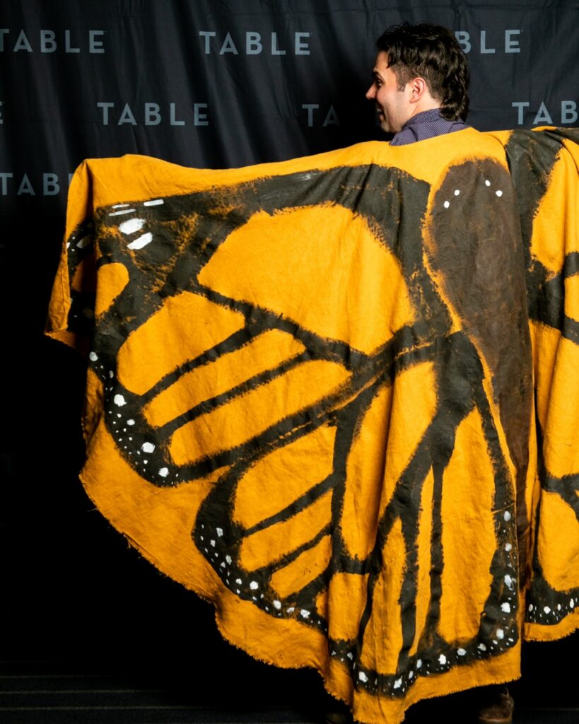 Man wearing a large, orange monarch butterfly wing costume.