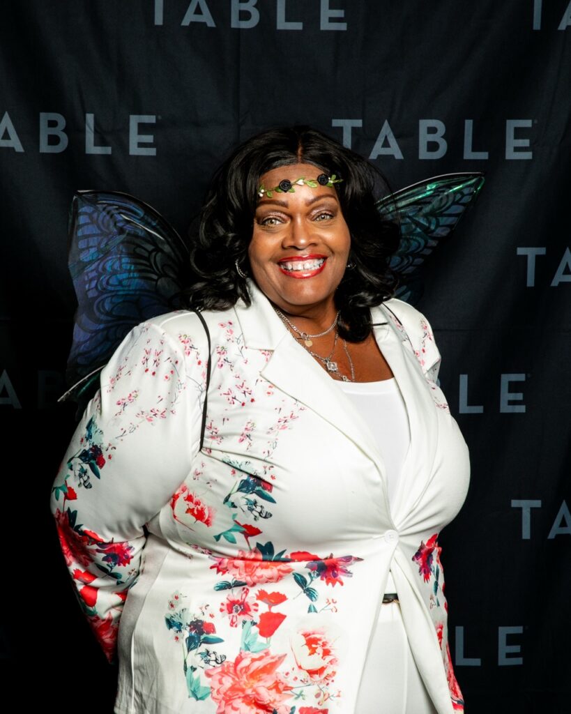 Plus-size Black woman in floral blazer and fairy wings smiles