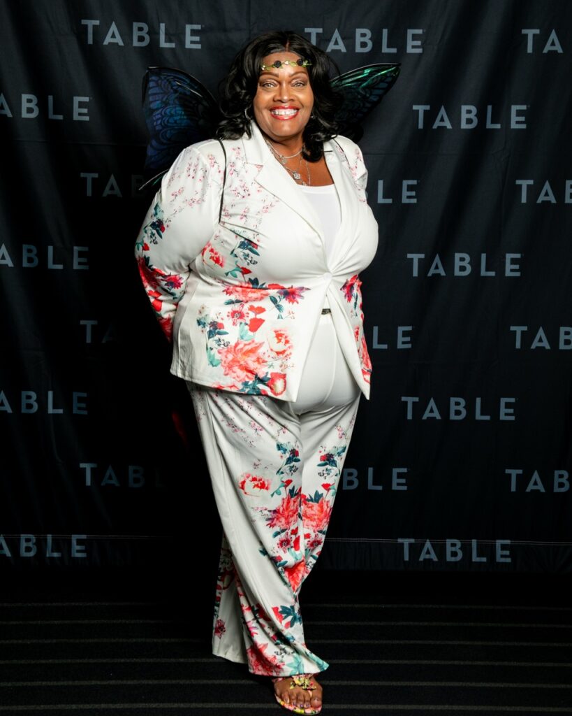 Plus-size woman in floral suit and fairy wings smiles at camera