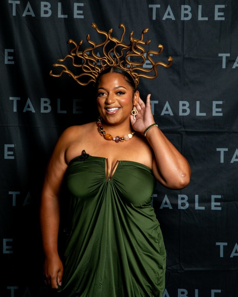 Woman in a green dress and Medusa costume smiles at the camera.