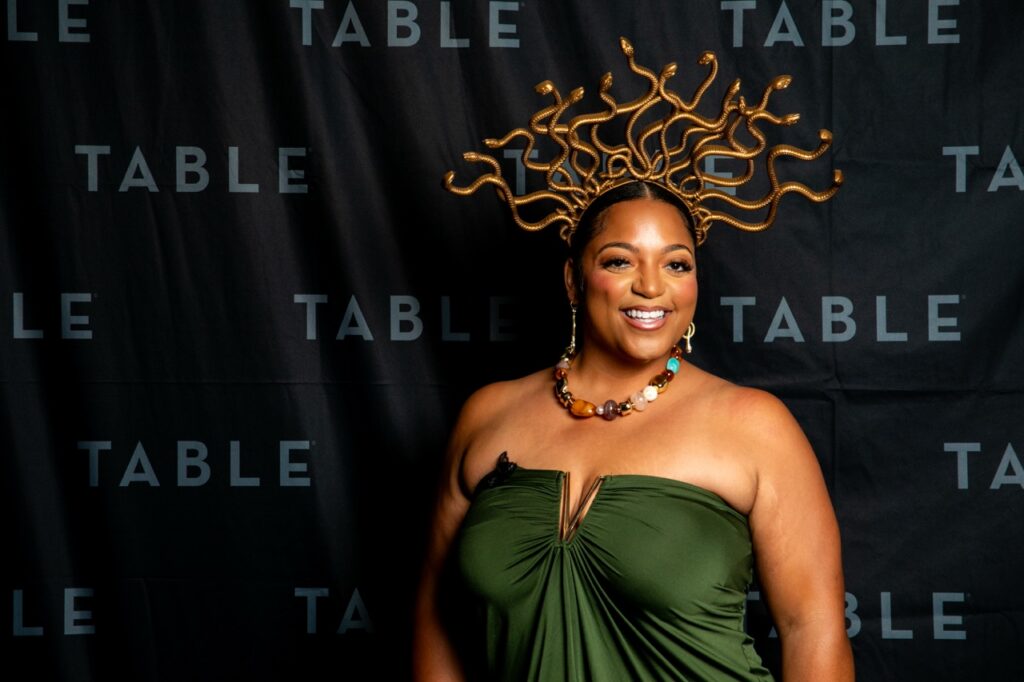 Woman in green dress and Medusa-inspired headpiece smiles