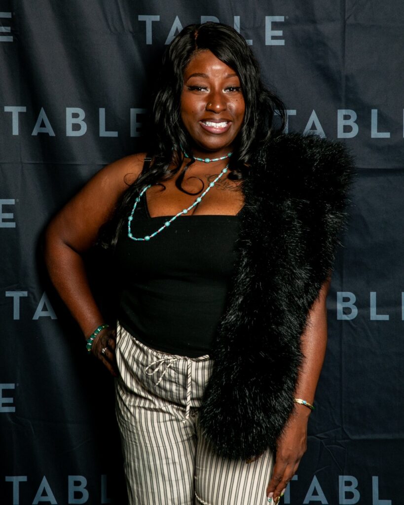 Woman in fur stole and striped pants smiles at the camera.
