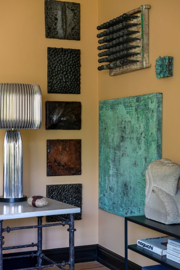 Gallery wall with metallic textured wall sculptures, green abstract painting, and fluted chrome lamp.
