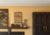 How Interior Stylist Danny Mankin Filled His Pittsburgh Home With Eclectic Decor Living room with black surround fireplace, dark wood cabinet, mantel artwork, and yellow paneled walls.