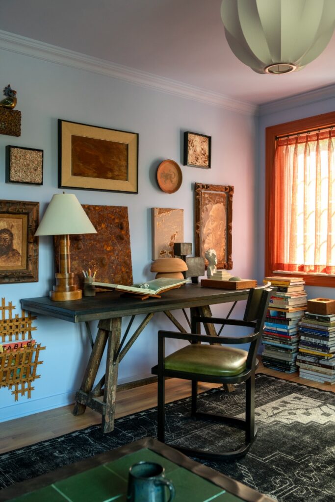 Home office featuring dark wood trestle desk, black armchair, gallery wall, and lavender-blue walls.
