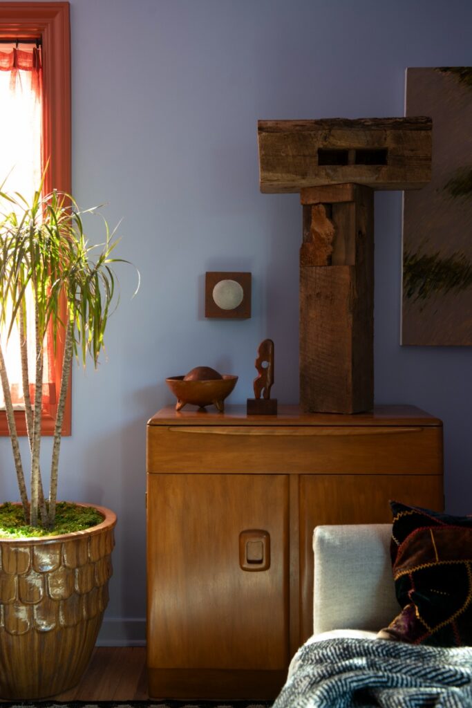 Mid-century wooden cabinet with abstract block sculpture and potted houseplant in textured ceramic planter.