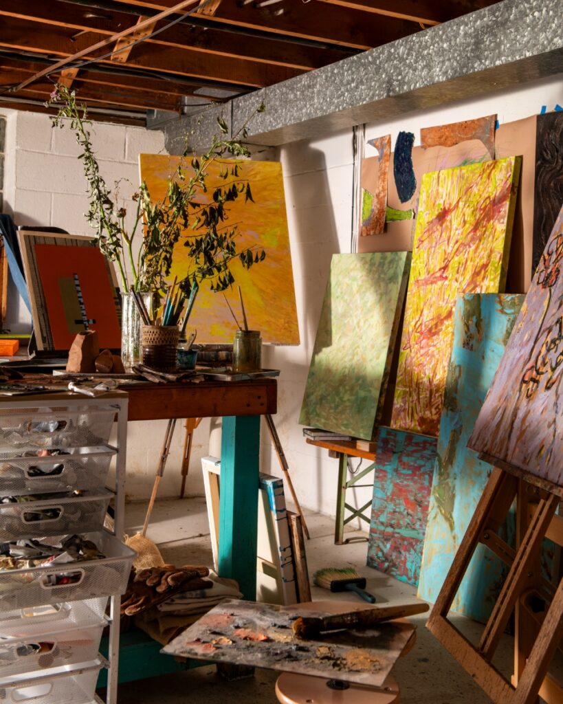 Artist studio filled with colorful abstract paintings on easels, paintbrushes, and art supply carts.