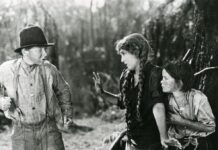 Pittsburgh Silent Film Festival Brings Classic Movies to Theaters This September Black-and-white film still from Sparrows showing Mary Pickford protectively shielding a child as an older boy in suspenders and a hat gesticulates in front of them outdoors.