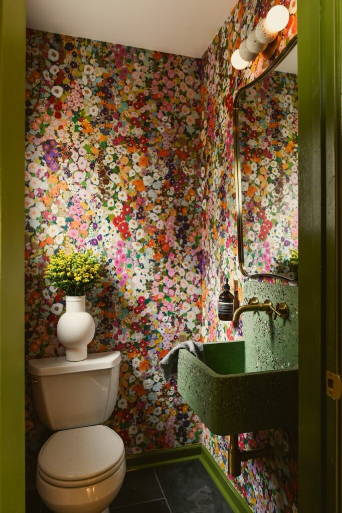 Bold powder room with floral wallpaper, green sink, and white toilet.