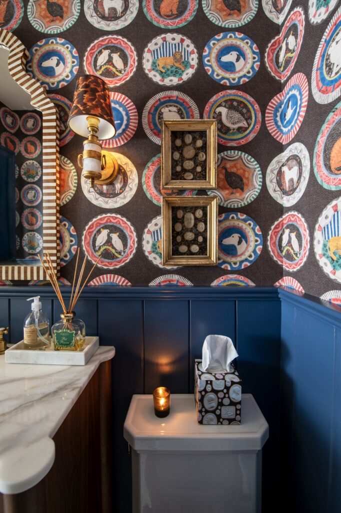 Bold powder room with patterned wallpaper, blue wainscoting, and decorative framed art.