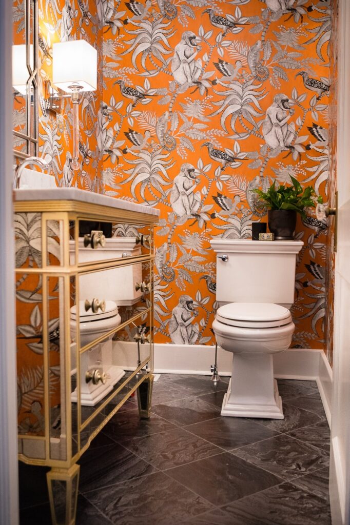 Bold powder room with orange monkey wallpaper and mirrored vanity