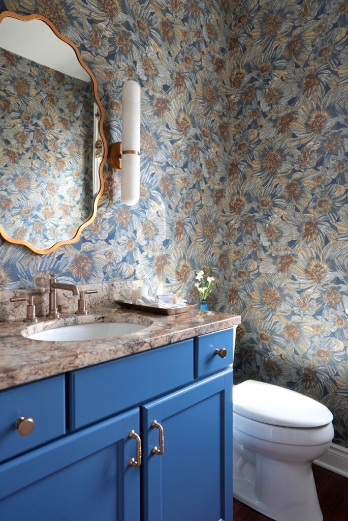 Bold powder room with blue vanity, floral wallpaper, and gold mirror