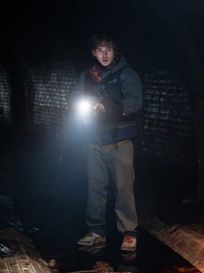 Austin Abrams traveling through a bloody dark tunnel with a flashlight in Resident Evil.