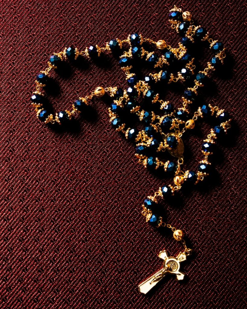 Gold and blue rosary beads with a cross pendant on a textured red background.