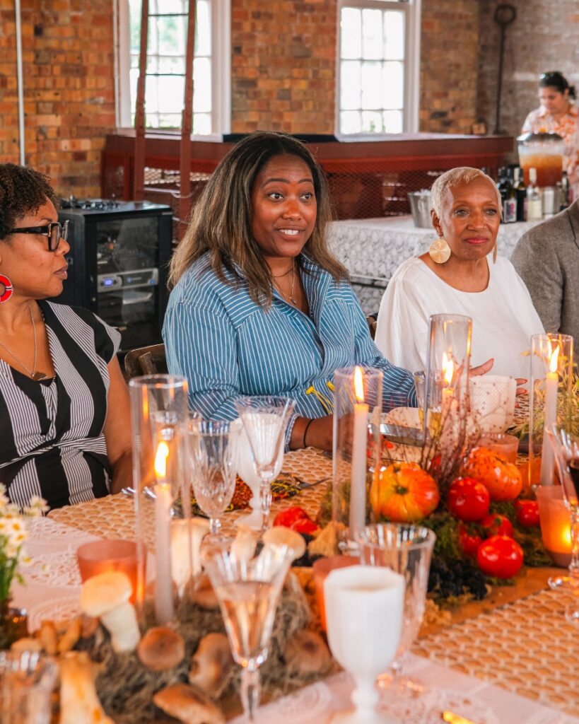 Nina Williams-Mbengue and guests seated at a decorated dining table with candles and fresh produce.