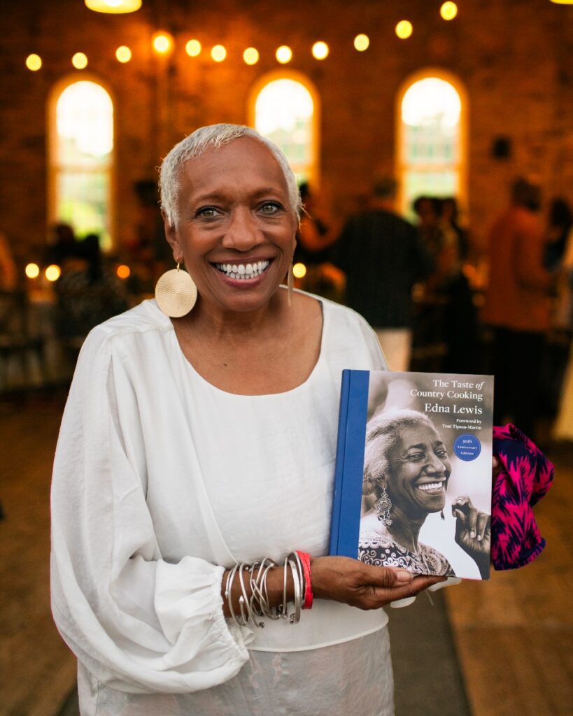 Nina Williams-Mbengue smiling while holding a copy of "The Taste of Country Cooking" cookbook.