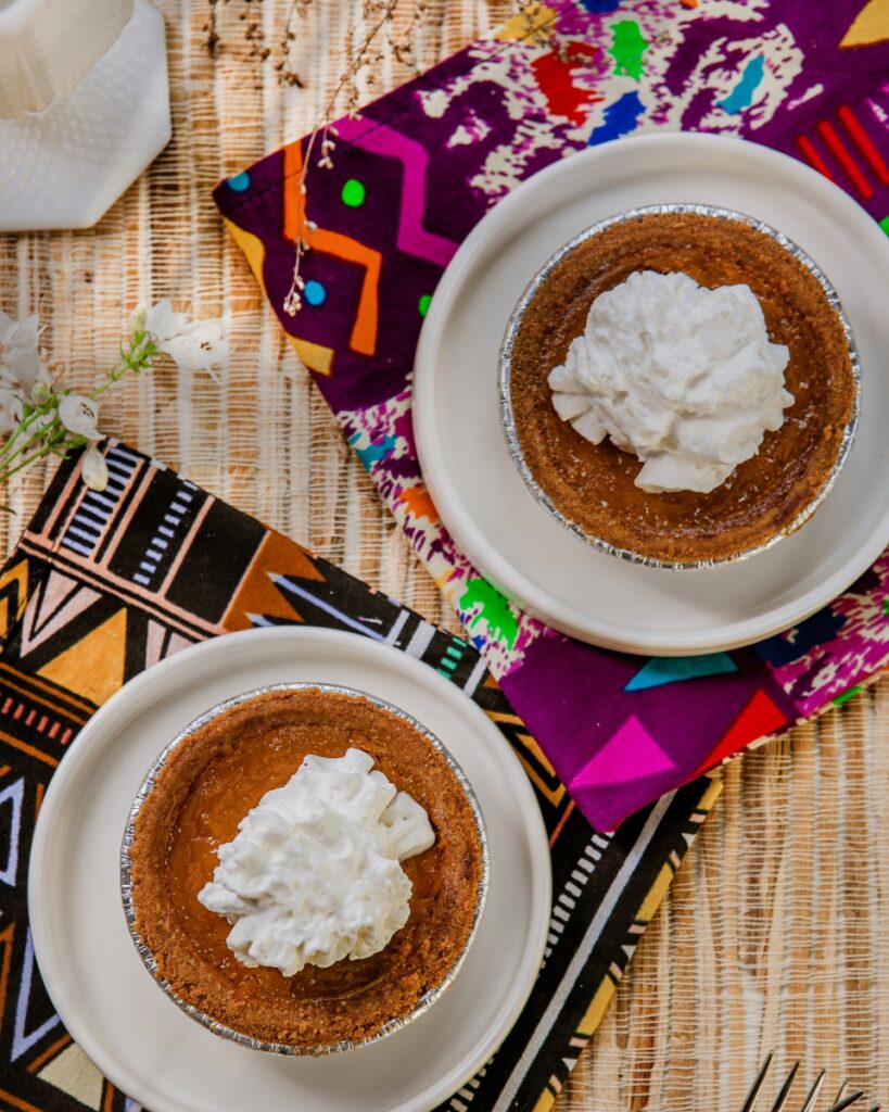 Top-down view of two individual sweet potato pies with whipped cream on decorative patterned fabric.