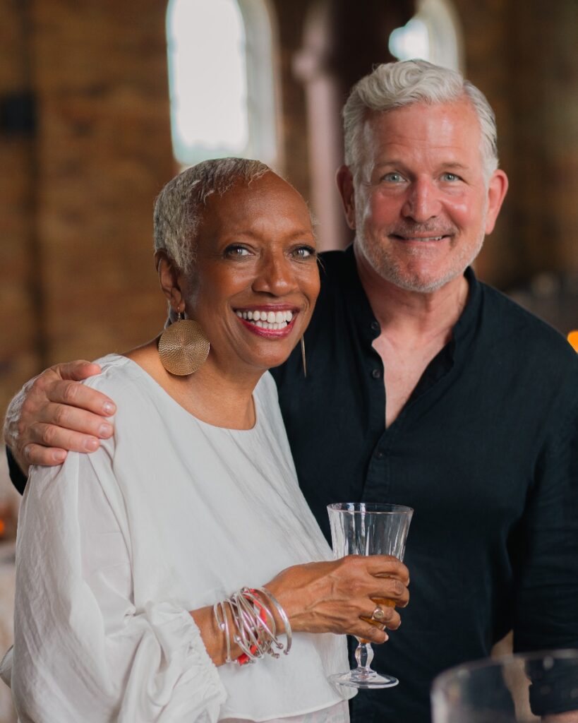 Nina Williams-Mbengue smiling next to Keith Recker while holding a cocktail at the Edna Lewis event.